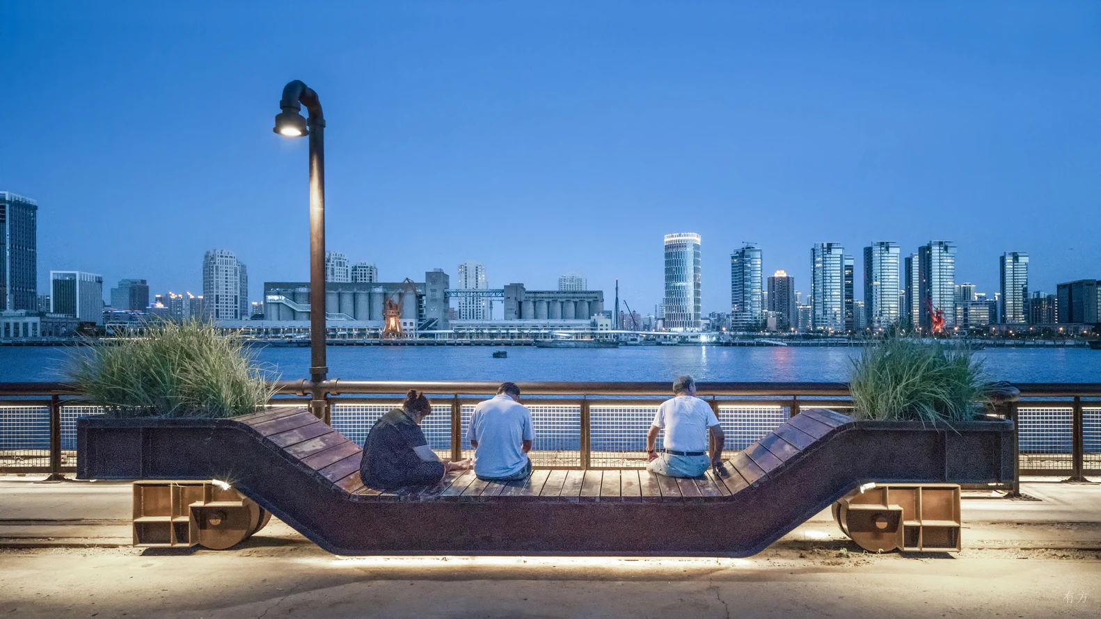 People gathering around an illuminated public bench on the Yangpu waterfront at dusk